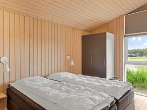 A bedroom with a wooden ceiling, two beds, a wardrobe, and a window with a view of greenery.