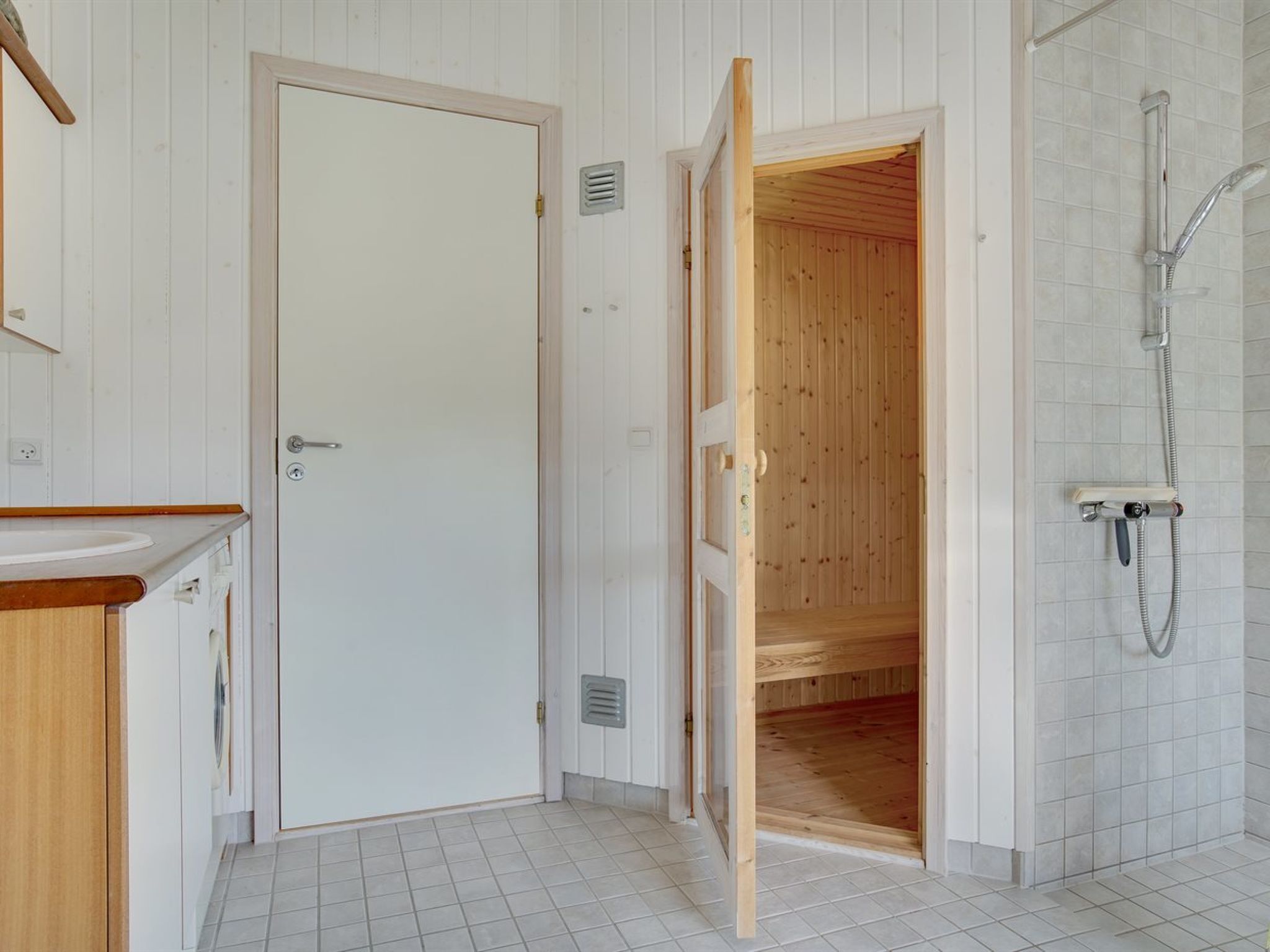 Een badkamer met een houten deur, een douche met handdouche en een betegelde vloer.
