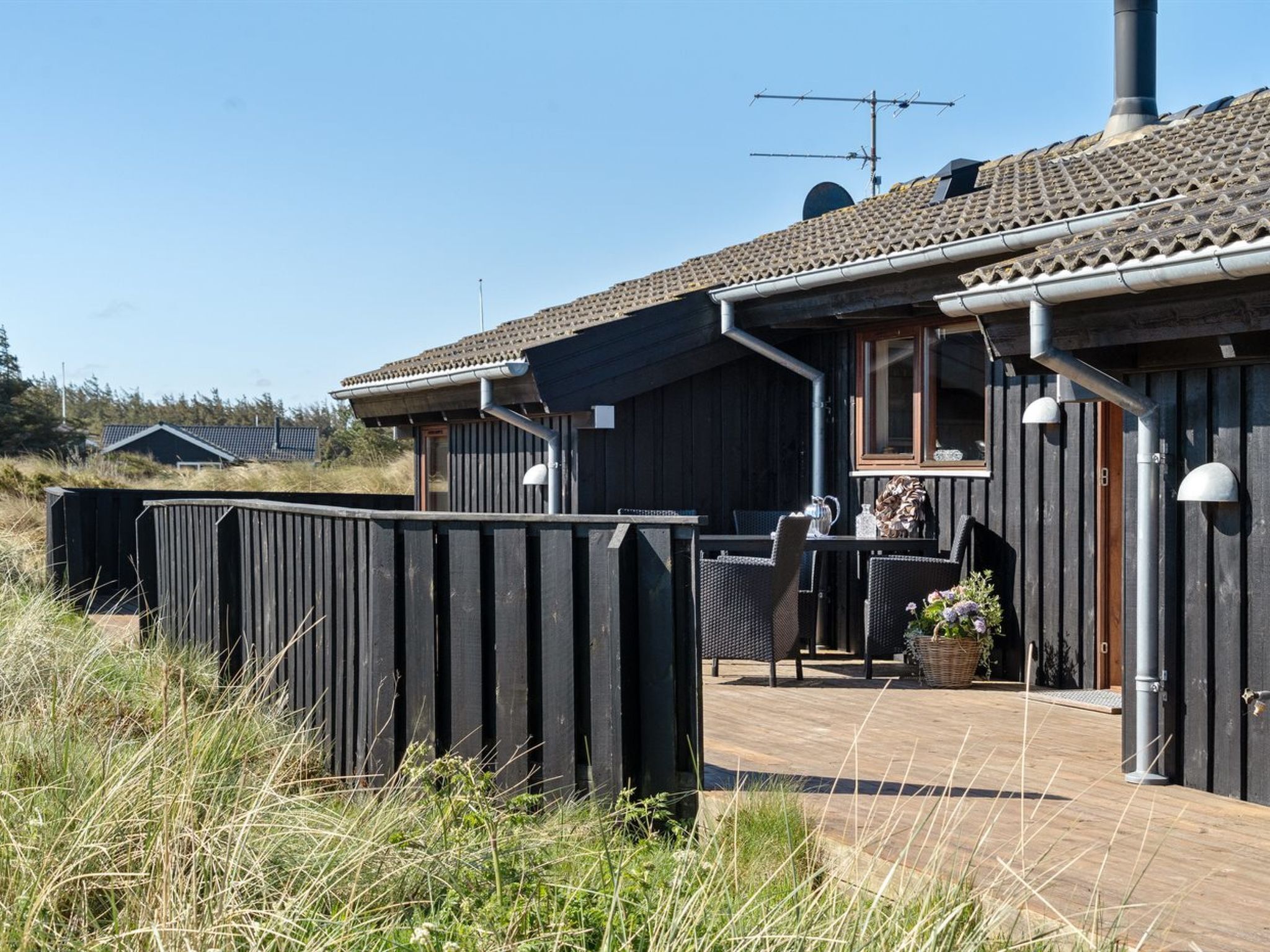 A wooden cabin with a tiled roof, a deck with outdoor seating, and a view of the surrounding landscape.