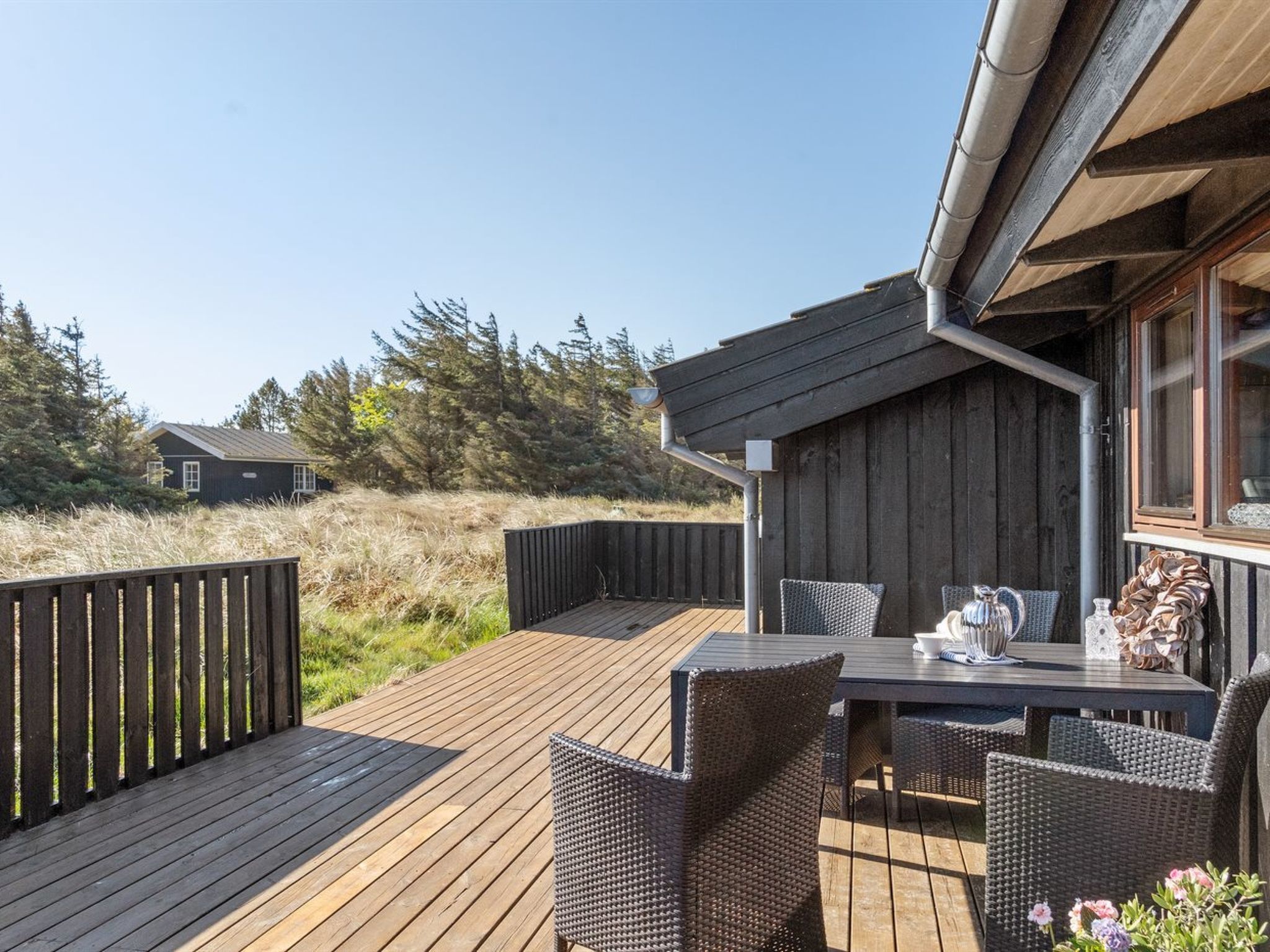 A wooden deck with wicker furniture and a table, overlooking a forested area.