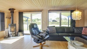 Ein modernes Wohnzimmer mit einem schwarzen Ledersessel, einem schwarzen Sofa, einem weißen Beistelltisch und einem Kaminofen.