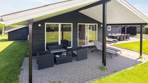 Eine moderne Terrassenausstattung mit überdachter Sitzgruppe, Feuerstelle und Blick auf den Garten.