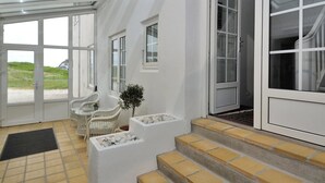A modern interior with large windows, a seating area with wicker chairs, and a staircase leading to an upper level.