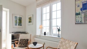 A cozy living room with a white sofa, two armchairs, a small round table, and a window with a view of a building.