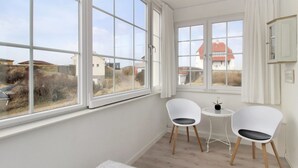 A room with large windows, two white chairs, a small round table, and a white rug.