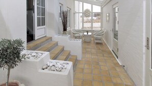 A modern interior with a glass ceiling, white walls, and a tiled floor. There are steps leading to a seating area with chairs and a table.
