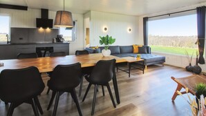 A modern living room with a wooden dining table, black chairs, a grey sofa, and a large window offering a view of the outdoors. - "Lok" - 450m from the sea by Interhome (Løkken)
