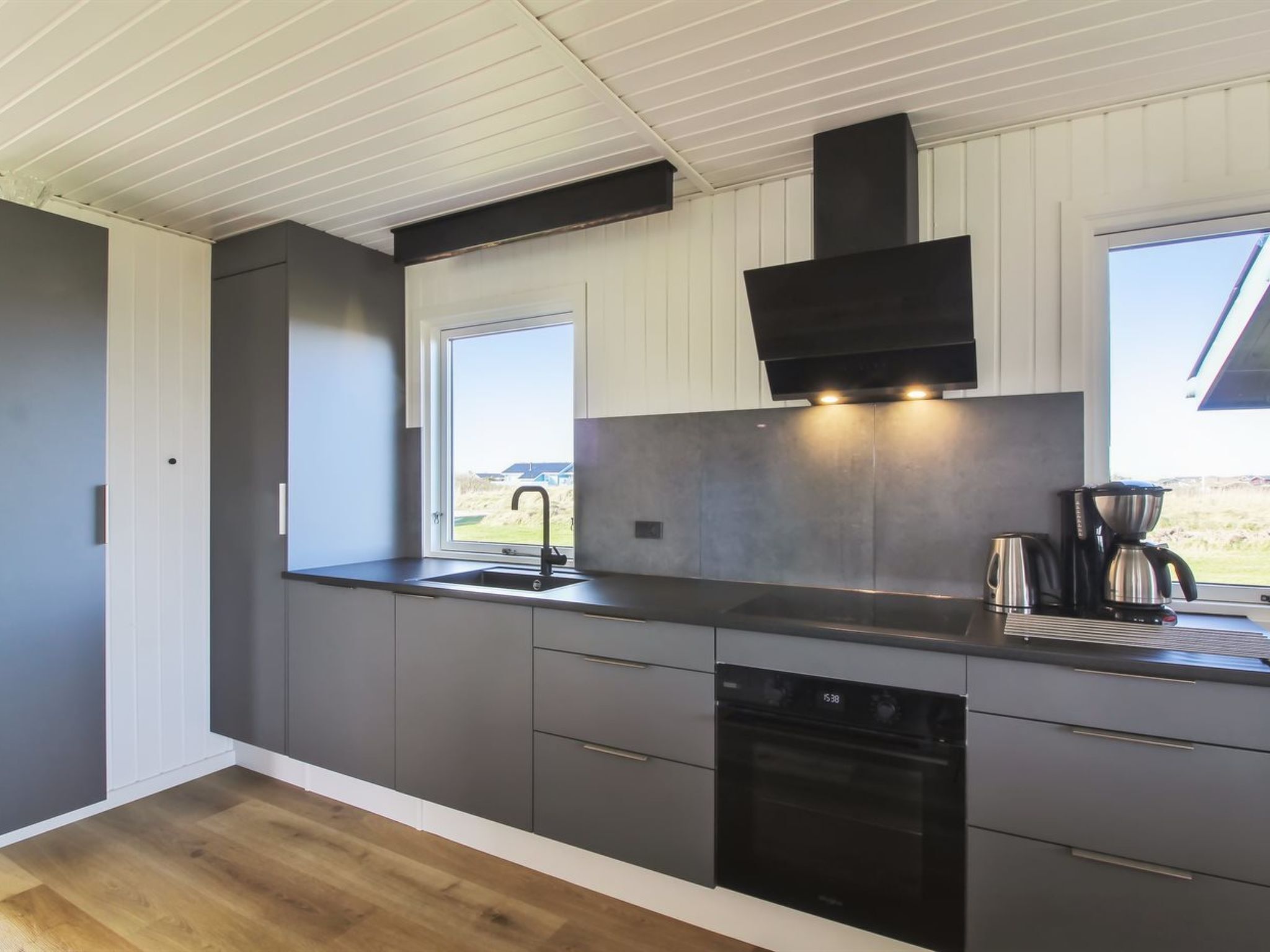 A modern kitchen with a black stove, a sink, and a window overlooking a grassy area.