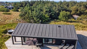 Une maison moderne avec un toit plat, de grandes fenêtres et une terrasse aménagée avec du mobilier d’extérieur.
