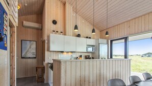 Une cuisine moderne avec un lambris en bois, un four à micro-ondes encastré et une grande fenêtre donnant sur un paysage verdoyant.