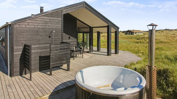 Une cabane moderne en bois dotée d’un patio couvert, d’un jacuzzi et d’un lampadaire en métal.