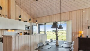Une cuisine moderne avec un lambris en bois, un coin repas avec une table et des chaises, et une vue sur l’extérieur.