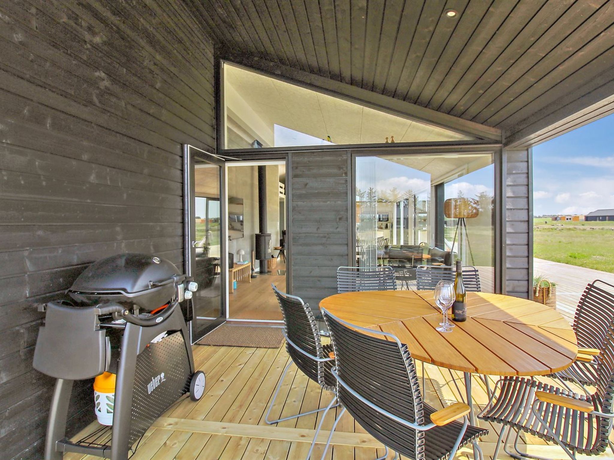 Een terras buiten met een barbecue, een tafel en stoelen.