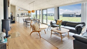 A spacious living area with a large window, a fireplace, and a modern kitchen in the background.