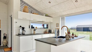 A modern kitchen with white cabinetry, a large island, and a view of the countryside.