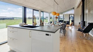 A modern kitchen with a large island, large windows, and a view of the outdoors.