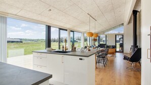 A modern kitchen with large windows, a central island, and a dining area with chairs.