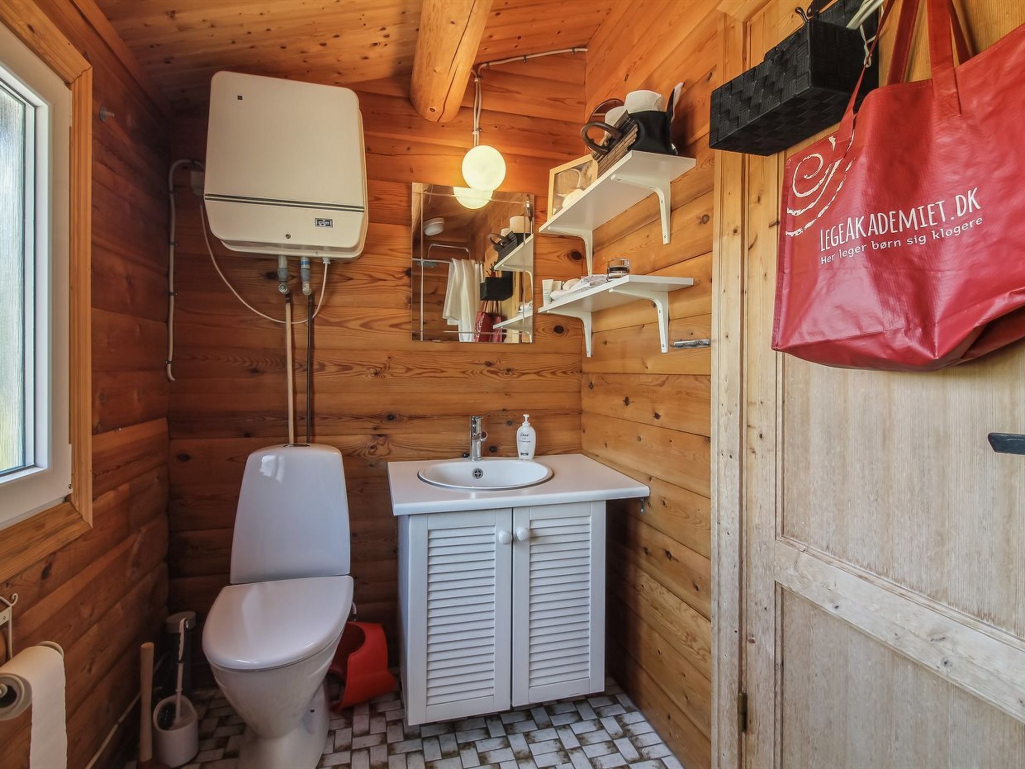 Een kleine houten badkamer met toilet, wastafel en spiegel.