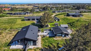 Une vue aérienne d'un quartier résidentiel avec des maisons modernes, un paysage verdoyant et une vue lointaine sur la mer.