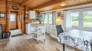 L’intérieur chaleureux d’un chalet en bois comprend une cuisine, un coin repas et de grandes fenêtres qui offrent une vue sur l’extérieur.