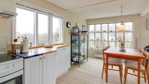 Une cuisine avec des meubles blancs, un plan de travail en bois, une table à manger avec des chaises et de grandes fenêtres.