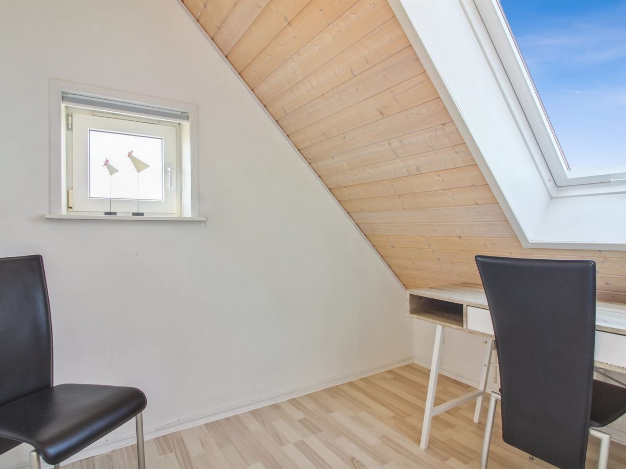 Una habitación con techo inclinado, tragaluz y dos sillas negras.