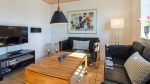 Una sala de estar moderna con techo de madera, un televisor de pantalla plana, un sofá de cuero negro, una mesa de centro de madera y un cuadro en la pared.