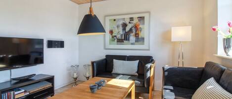 A modern living room with a wooden ceiling, a flat-screen TV, a black leather sofa, a wooden coffee table, and a painting on the wall.