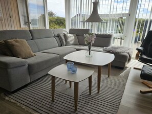 A modern living room with a grey sofa, two white tables, and a black chair.