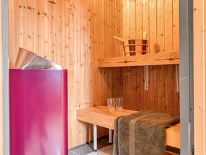Uma sauna de madeira com um banco de madeira, uma mesa com copos e um armário rosa.