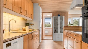 Une cuisine moderne avec des meubles en bois, un plan de travail en granit, des appareils électroménagers en acier inoxydable et une vue sur l’extérieur grâce à une porte vitrée.
