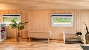 Une pièce aux murs lambrés, avec un banc, une plante, une bibliothèque et deux fenêtres.