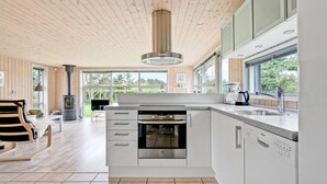 A modern kitchen with a built-in oven, a dishwasher, and a large window providing a view of the outdoors. - "Into" - 400m from the sea by Interhome (Løkken)