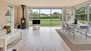 A modern living room with a wood-burning stove, a dining area with a table and chairs, and large windows offering a view of the outdoors. - "Into" - 400m from the sea by Interhome (Løkken)