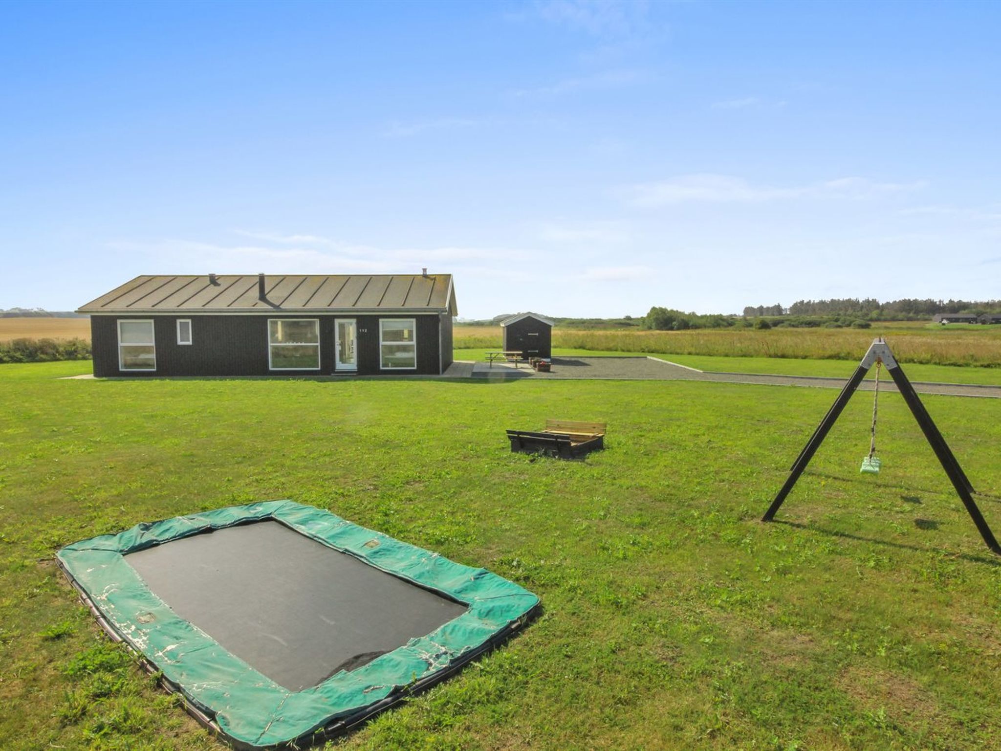 A grassy field with a trampoline, a small shed, and a house with a metal roof.