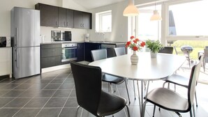 Una cocina moderna con armarios oscuros, electrodomésticos de acero inoxidable y un comedor con una mesa redonda y sillas.