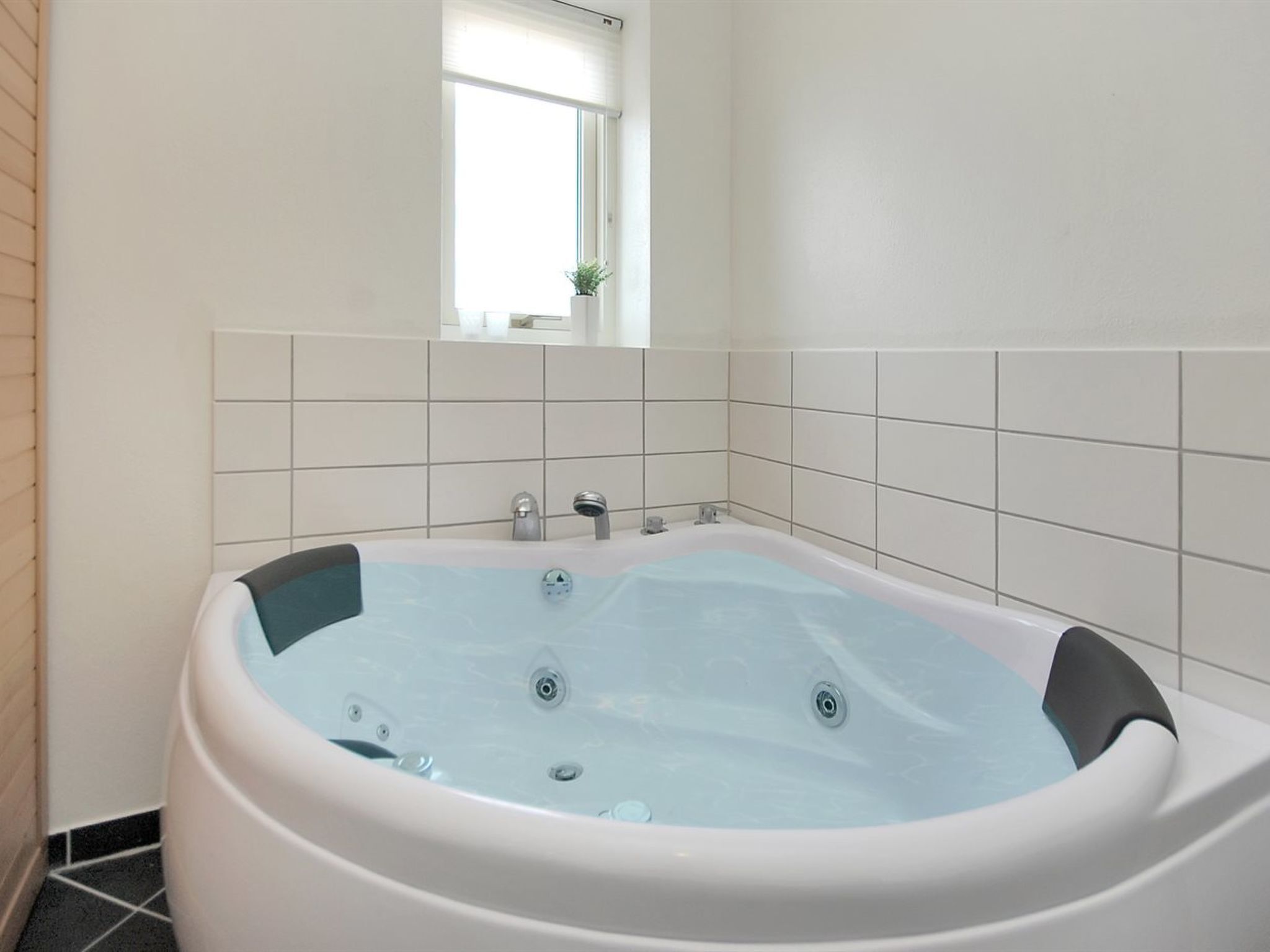 A modern bathroom with a freestanding bathtub, white tiled walls, and a window providing natural light.