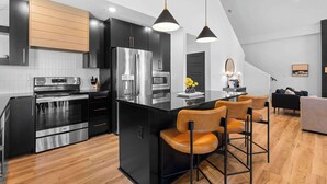 Une cuisine moderne dotée d’un îlot central, d’appareils électroménagers en acier inoxydable et de luminaires suspendus.