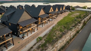 Une rangée de cabanes modernes aux toits sombres, dotées de coins salon extérieurs, se dressant sur fond de lac et de coucher de soleil.
