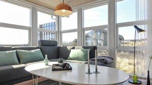 Ein modernes Wohnzimmer mit einem grauen Sofa, einem weißen Couchtisch und einem großen Fenster mit Blick auf Gebäude.