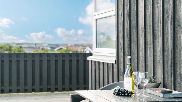 Eine Holzterrasse mit Tisch für zwei Personen, komplett mit einer Weinflasche, Gläsern und einer Oliven-Schale.