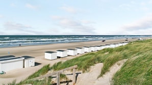 Ein Ferienanwesen direkt am Strand mit mehreren weißen Hütten, die entlang der Küste liegen, einem Sandweg, der zum Strand führt, und dem Meer im Hintergrund.