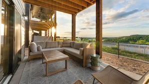 A covered outdoor seating area with a sofa, tables, and a view of a river and greenery. - Lakeview! Indoor Pool! Pool Table! (Hollister)