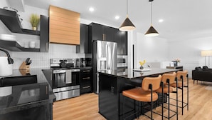 A modern kitchen with black cabinetry, stainless steel appliances, and a central island with bar stools. - Lakeview! Indoor Pool! Pool Table! (Hollister)