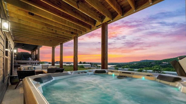 Ein Whirlpool unter einer Holzpergola mit Blick auf einen Sonnenuntergang über einer hügeligen Landschaft.