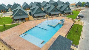 Un resort con varias construcciones de estilo chalet, una piscina central y vistas a un lago.