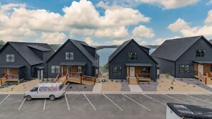 Une rangée de cabanes modernes aux couleurs sombres, dotées de balustrades en bois, un parking et un ciel dégagé.