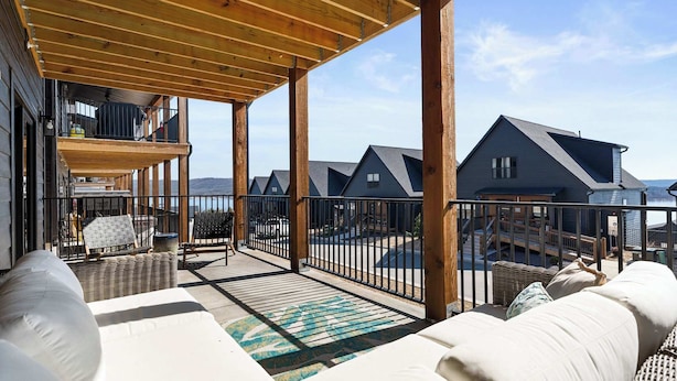 Un espace extérieur abrité, doté d'une terrasse en bois, de meubles en osier et offrant une vue sur plusieurs maisons.