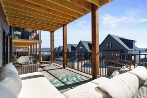 A covered outdoor area with a wooden deck, wicker furniture, and a view of multiple houses.