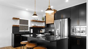 Une cuisine moderne avec des meubles de couleur noire, des appareils en acier inoxydable, un îlot central doté de tabourets et un éclairage suspendu.